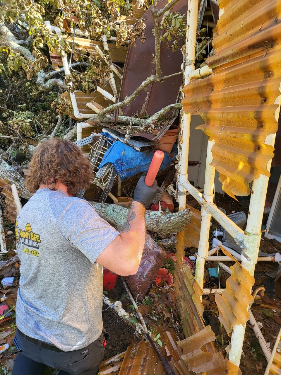 Robert reaching exposed outdoor plumbing surrounded by tree debris